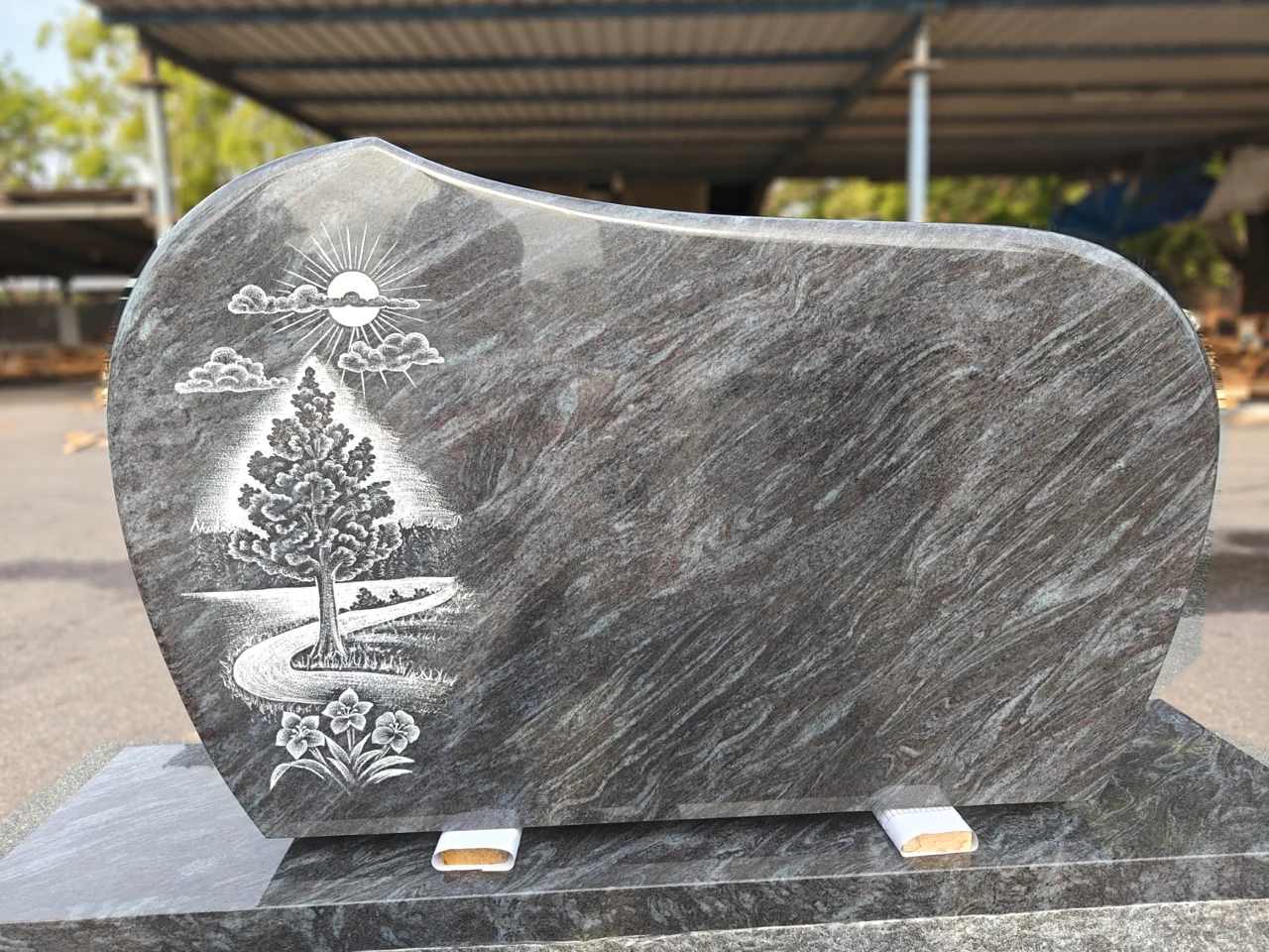 Tree, sun, winding path and flowers etched on a sweeping-top granite monument
